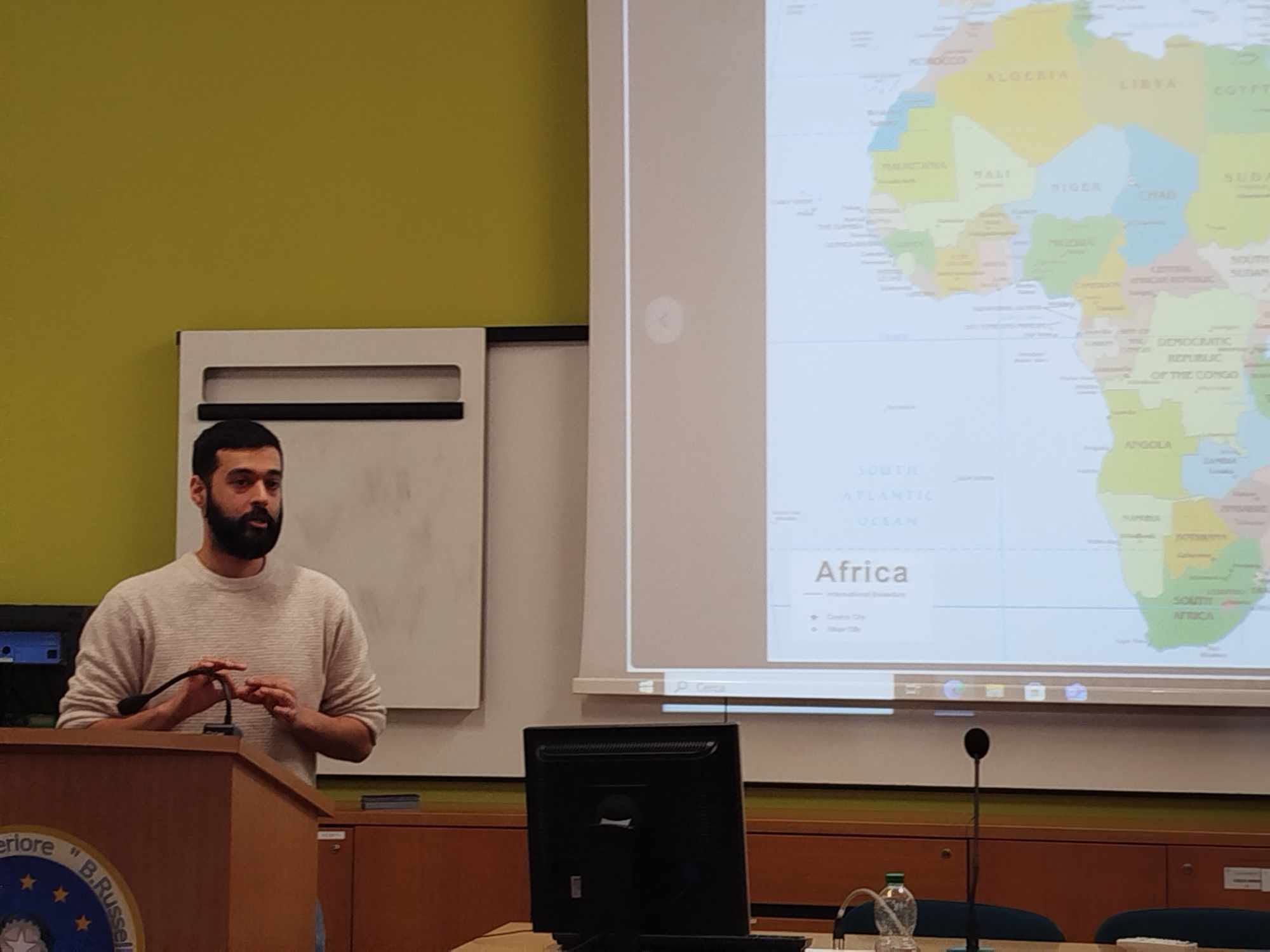 Sarvish Waheed parla davanti a una carta dell'Africa durante un incontro con le scuole superiori di Guastalla